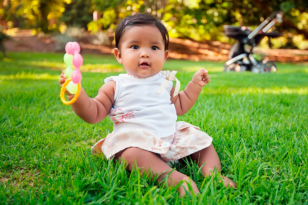 A cute baby sits on a grassy field, joyfully holding a colorful rattle creating a warm and cheerful atmosphere.